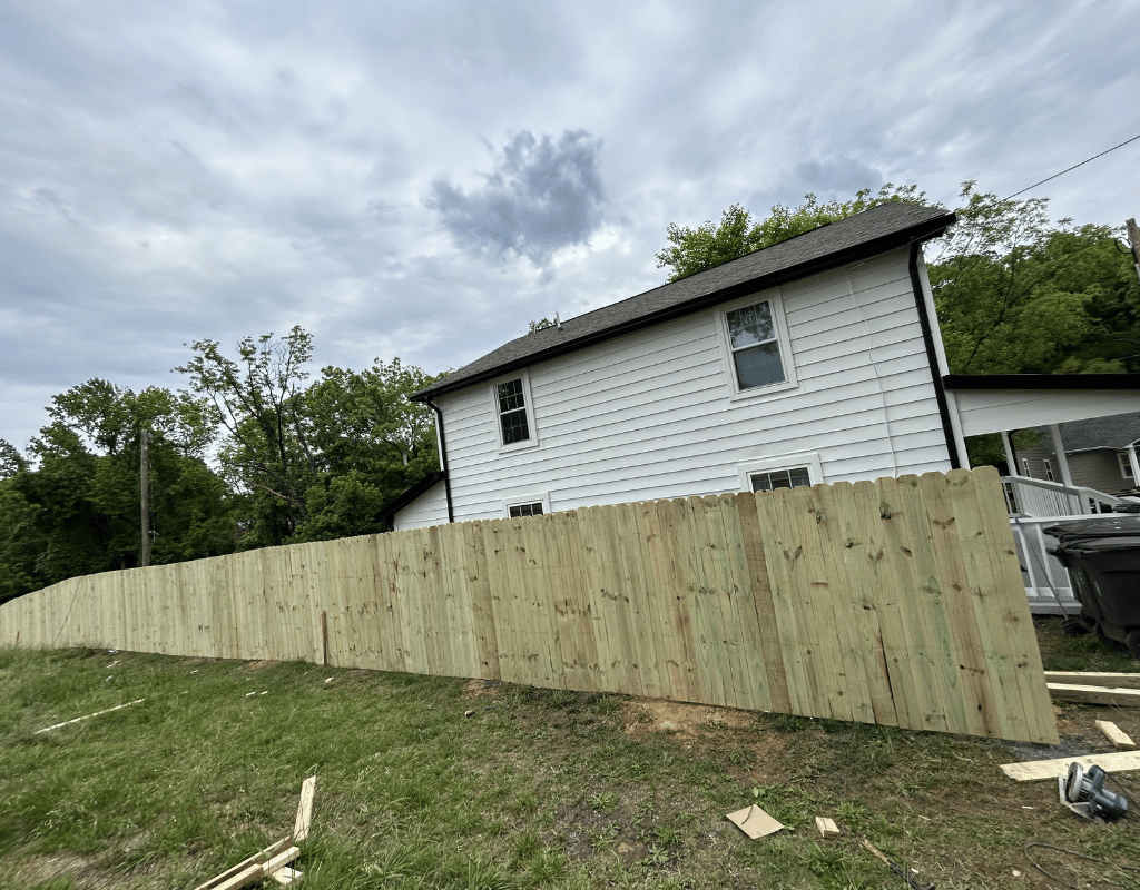 Wood privacy fence being installed on a sloped, wooded residential lot