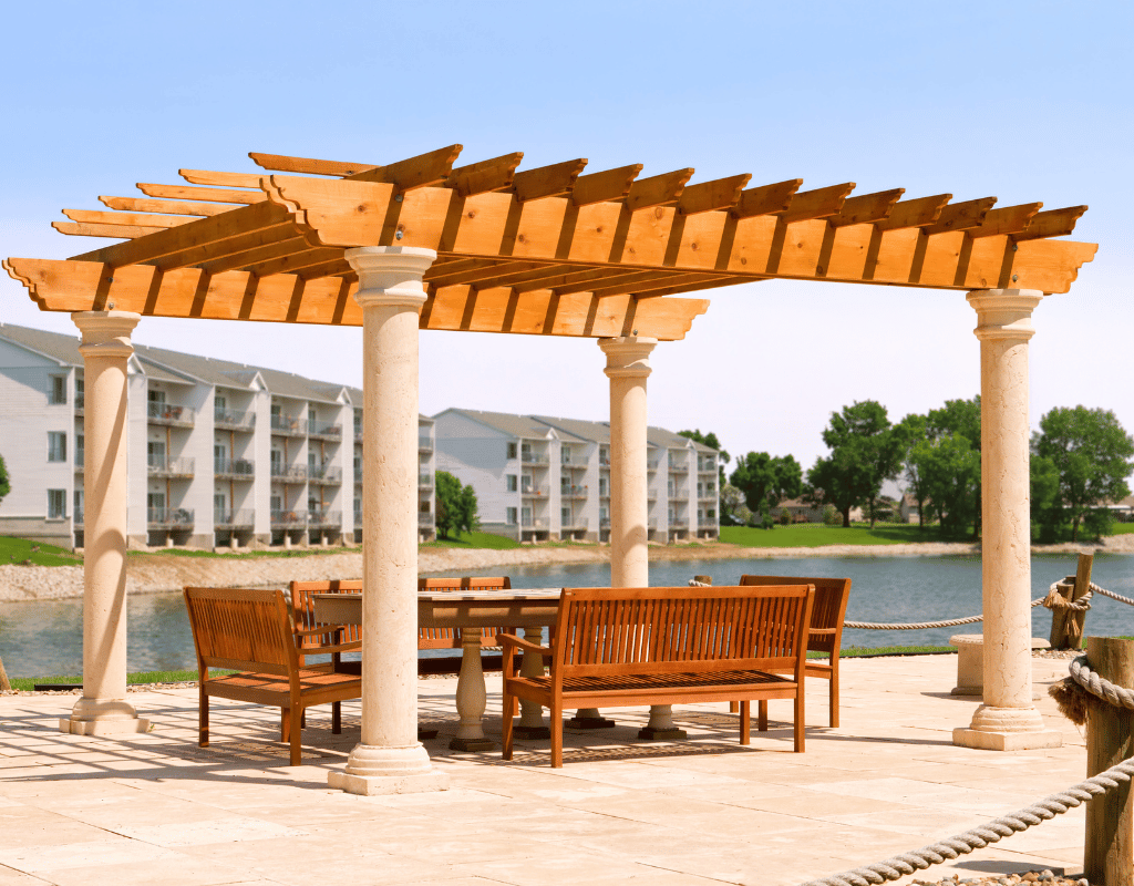 Wood pergola with stone columns shading a patio seating area beside a lake