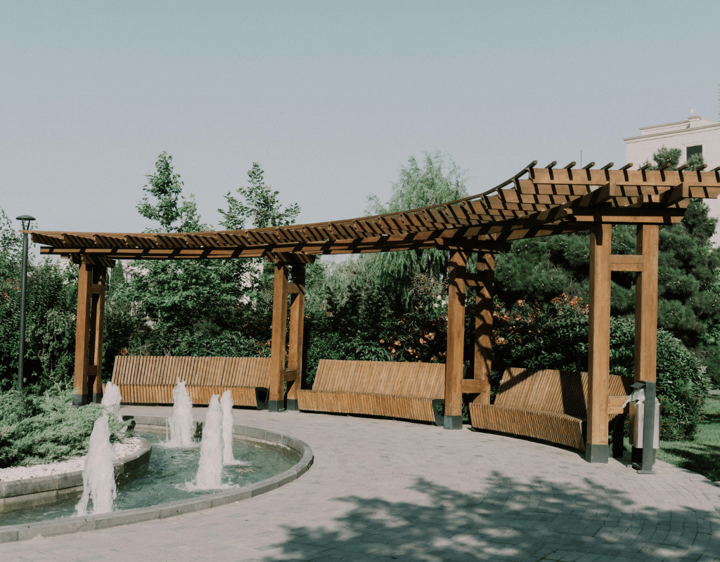 Wood pergola shading a curved bench beside a fountain in a landscaped courtyard