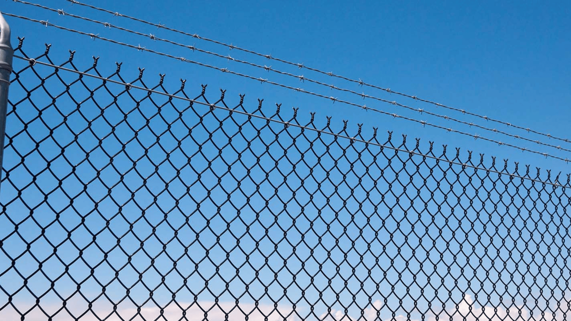 Chain link fence topped with barbed wire against a blue sky