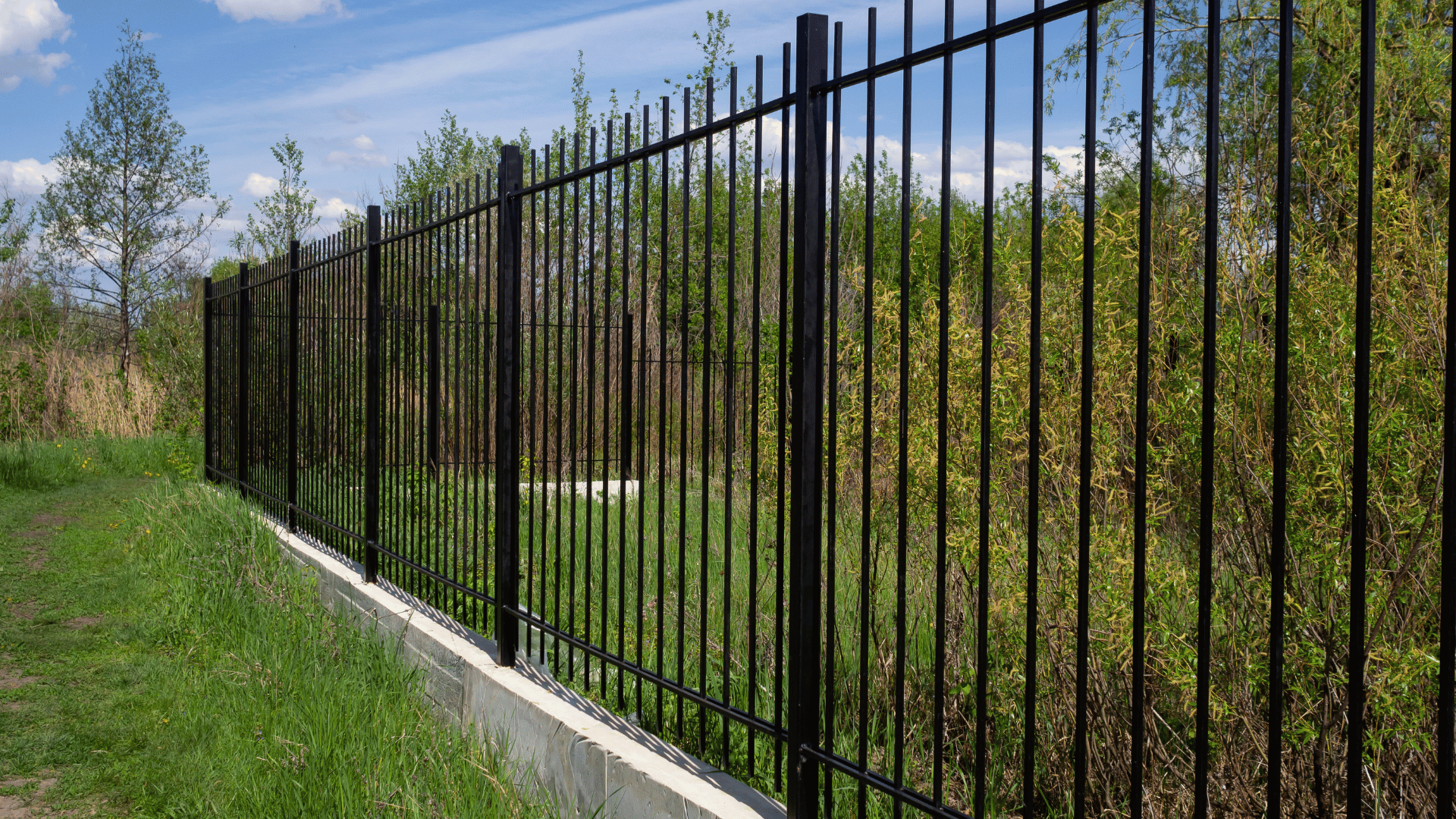 Black aluminum commercial fence installed along a grassy embankment near trees