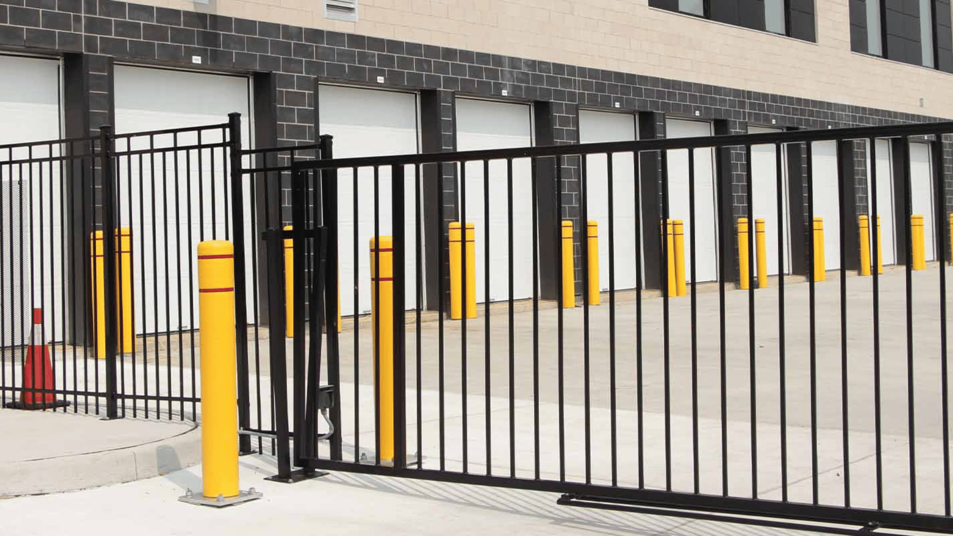 Black metal commercial sliding gate with yellow safety bollards at a loading dock