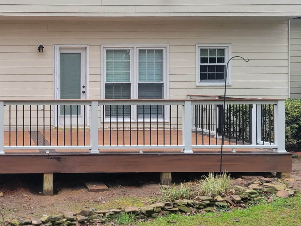 Wood deck with white columns and black metal railing on a home's front porch