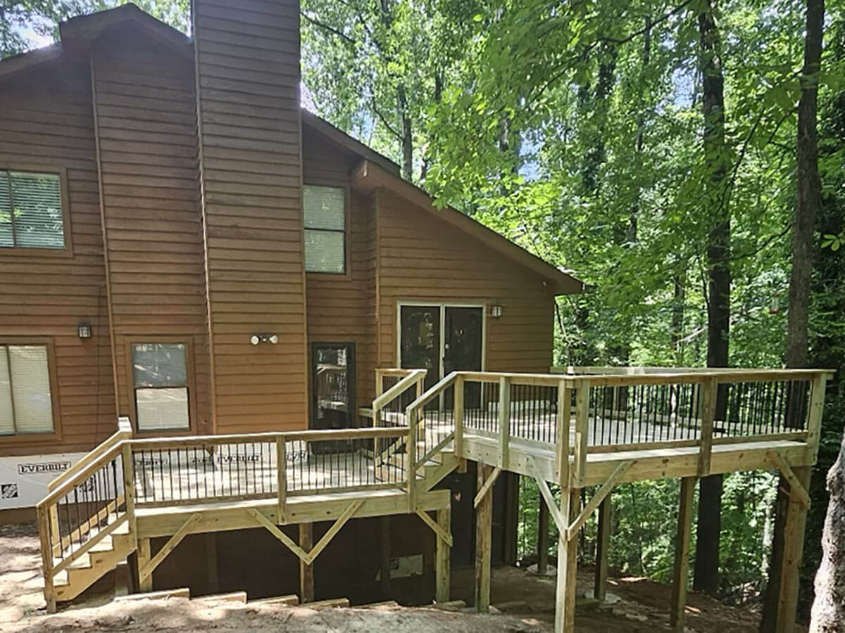 Newly built wood deck with black metal railing attached to a cabin in the woods