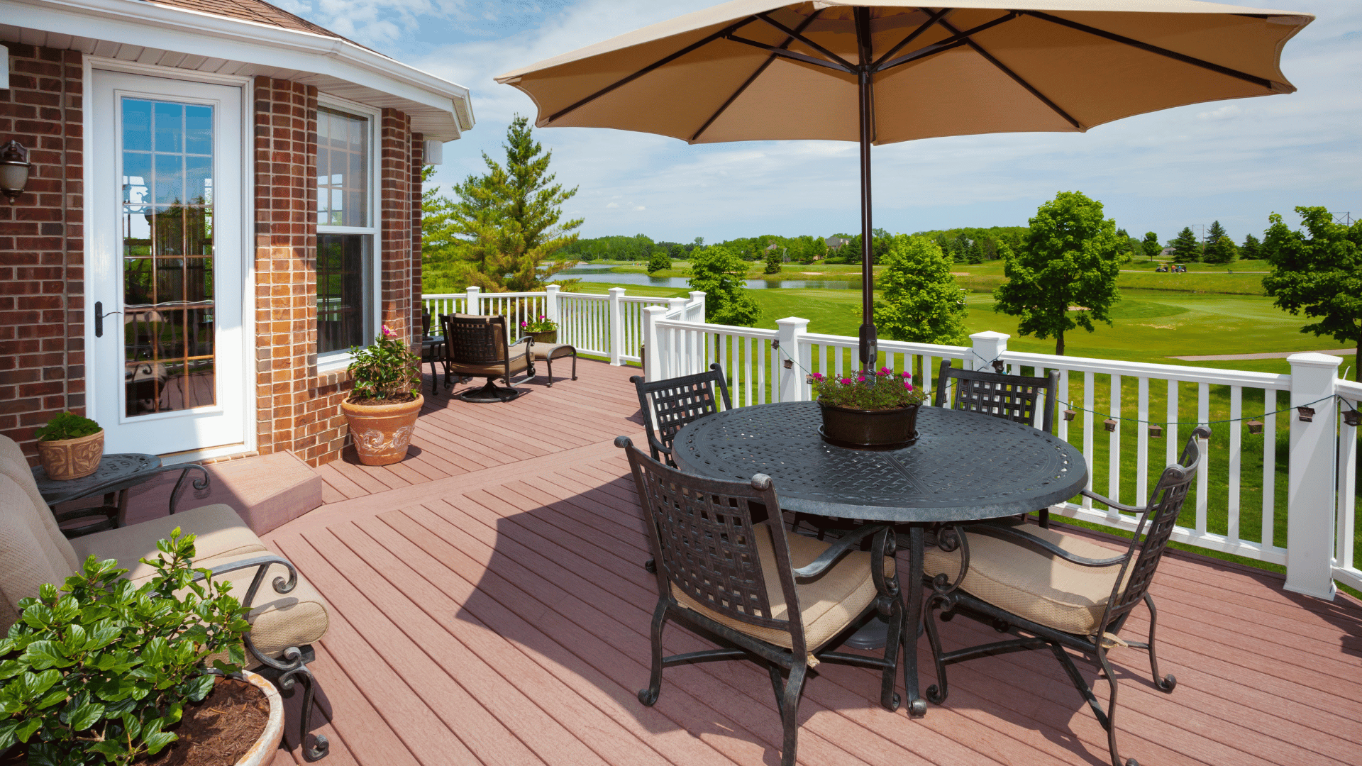 Composite deck with patio furniture and umbrella overlooking a golf course and lake