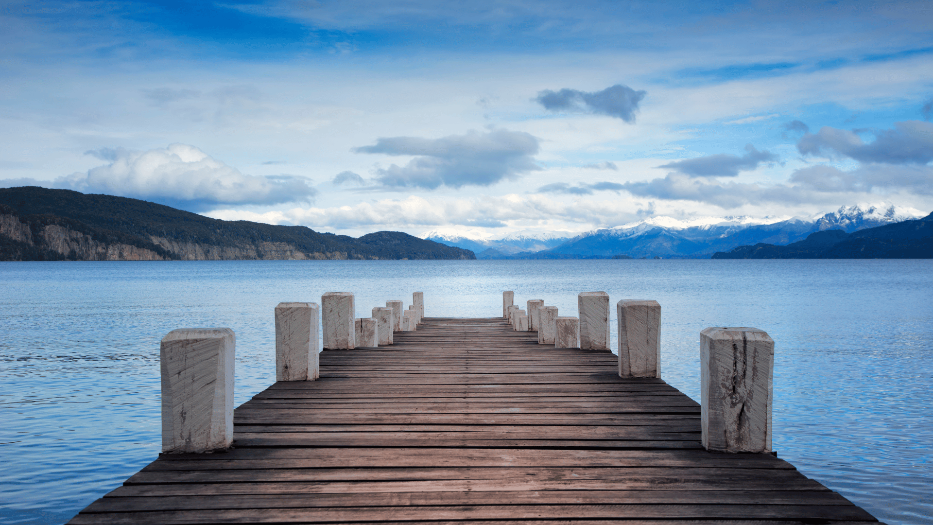 Wood dock extending into a blue lake with mountains in the background