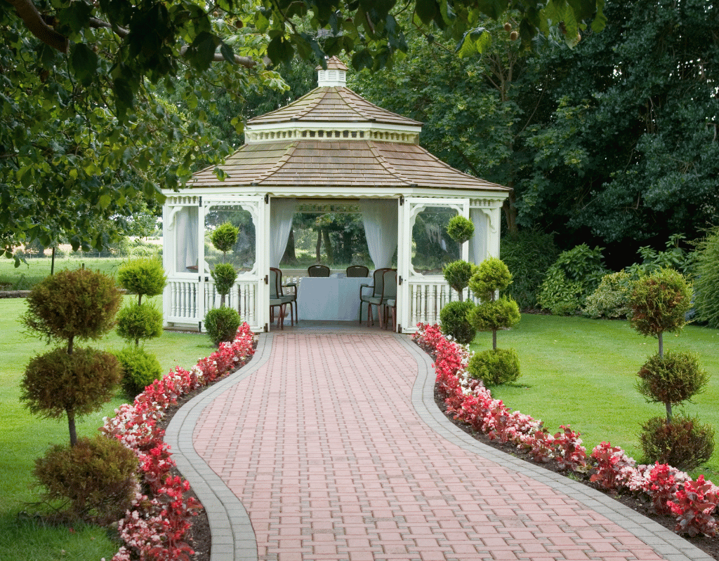 White gazebo with a shingled roof at the end of a flower-lined garden path