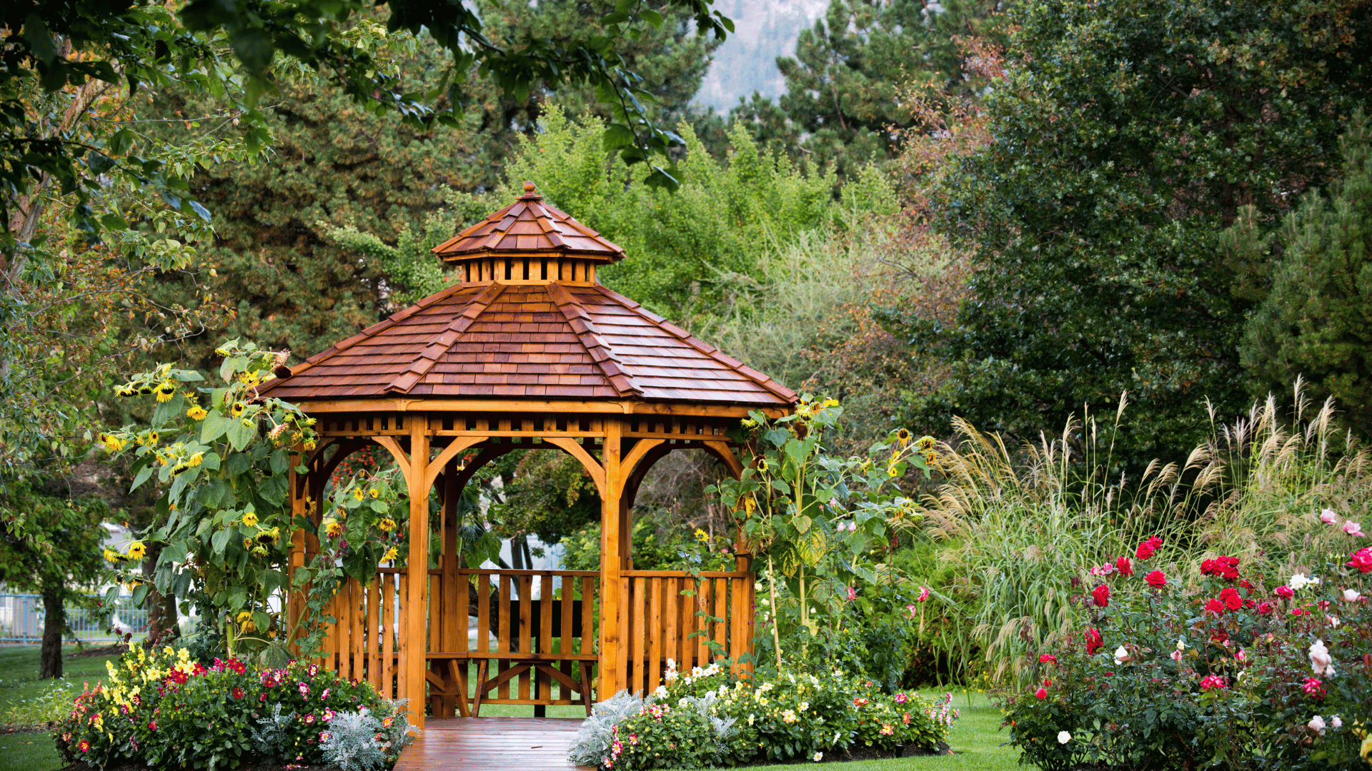 Wood gazebo with a cedar shingle roof surrounded by colorful garden flowers