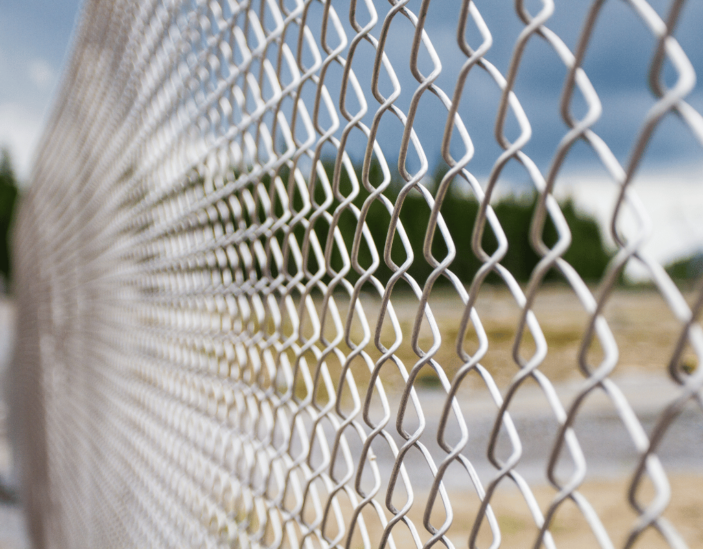 Close-up view of a silver chain link fence with an open field in the background