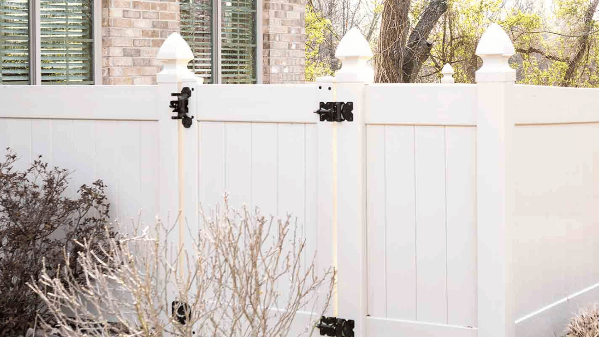 White vinyl privacy fence with black hardware alongside a brick home