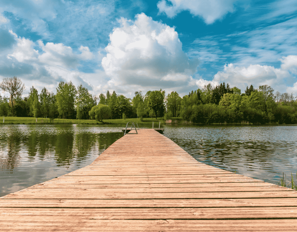 Wooden lake dock with a metal swim ladder under a cloudy sky